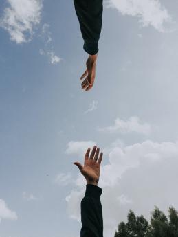 One arm and hand is reaching up towards another hand and arm reaching down.againsst the backdrop of a cloudy sky.