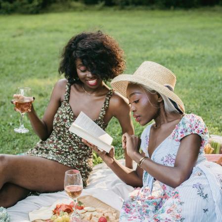 Two women reading outside at a picnic with floral dresses