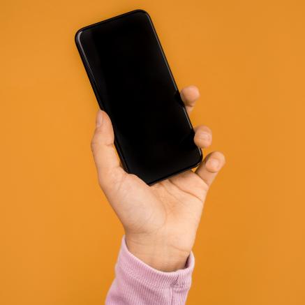 An arm in a pink sleve holds an iphone against a dark yellow background.