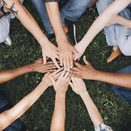 People of varying races putting their hands in the middle signifying teamwork