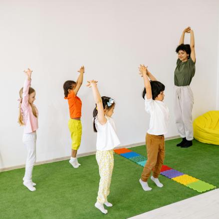 Kids stretch on green grass rug inside