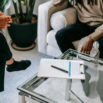 People's legs on the couch as they talk over forms on a clipboard