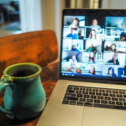 A laptop displaying a video call, next to a mug on a table.