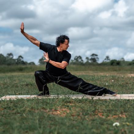 A man wearing a black Tai Chi Uniform poses in a field.