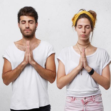 A man and a woman stand in a yoga pose.