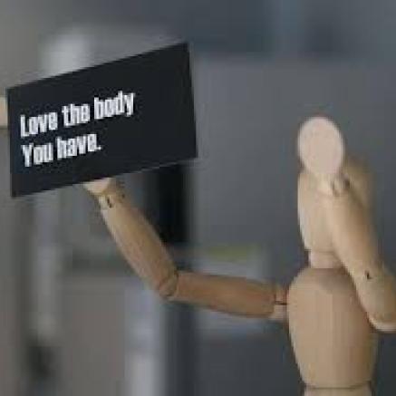 a wooden art figure holding a sign that reads love the body you have