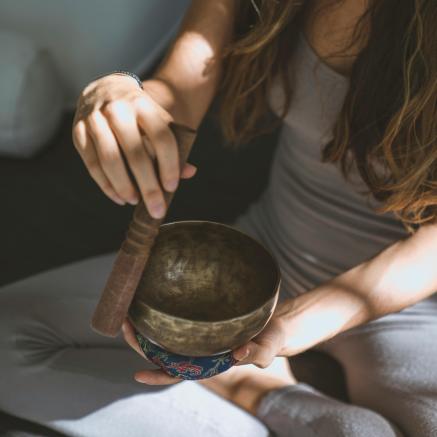 A woman is sitting cross legged with a tibetan singing bowl.