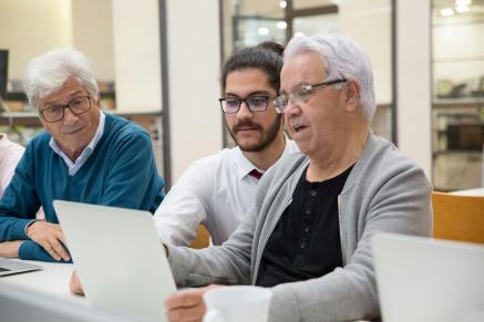 An older man and woman sit in front of laptop computers with a younger man.