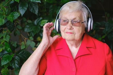 An older woman in a red shirt listens to her headphones.