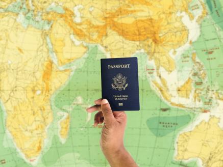 A hand holds up a US passport in front of a world map