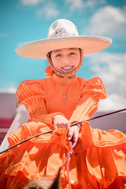 A Mexican girl in a colorful dress looks at the camera.