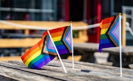 Three miniture inclusive (LGBTQ) flags on a picnic table.