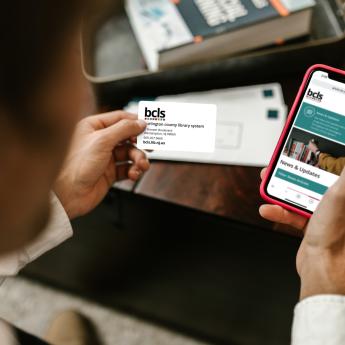 Person holding a BCLS library card and a cell phone with the BCLS Mobile website