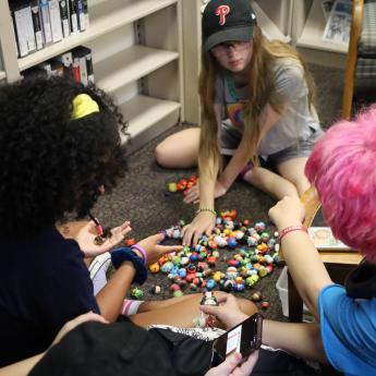 Three teens play with small Disney figurines at Riverton Anime Club