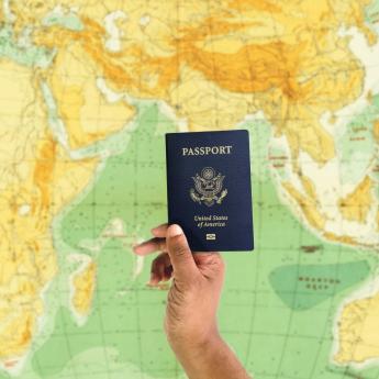 A hand holds up a US passport in front of a world map