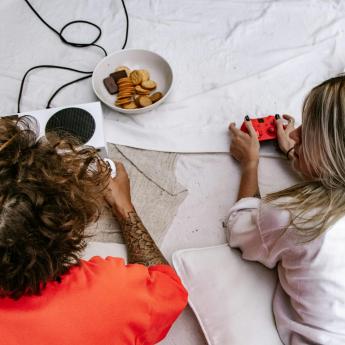 Two people lay on their stomachs on blankets with gaming controllers